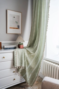 Détail de rideau en lin vert avec broderie blanche et pompons décoratifs de couleur crème
