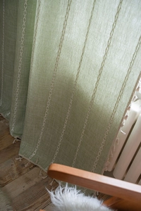 Detail eines grünen Leinenvorhangs mit weißer Kreuzstickerei und Fransenquasten