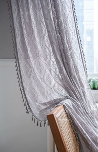 Close-up of grey crochet lace curtain with tassels and floral jacquard patterns