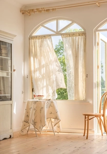 Close-up of semi-sheer linen curtain and matching floral tablecloth in sunlit room
