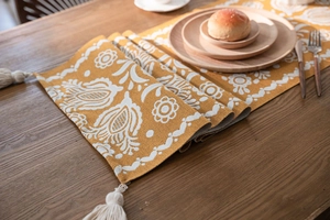 Detail of jacquard table runner with yellow floral patterns and white cotton tassels