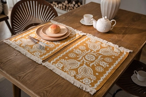 Detail of yellow woven table runner with white jacquard floral patterns and cotton tassels