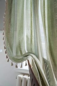 Détail du tissu de rideau vert en coton et lin avec rayures et pompons beige