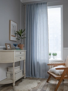 Dettaglio della tenda in lino azzurro con ricami geometrici e nappe beige