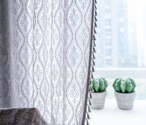 Detail of grey hollow-out crochet curtain with geometric floral patterns and tassel fringe