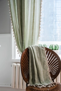 Détail d'un rideau vert texture lin avec des glands crème et des motifs géométriques