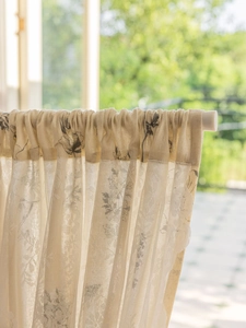 Detail of floral printed linen cafe curtain with rod pocket design in a sunlit garden setting