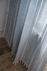 Close-up of blue linen curtain with geometric embroidery and white tassel trim