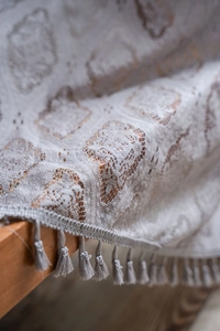 Detail of grey crochet lace curtain fabric with geometric patterns and tassel trim