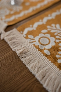 Detail of mustard yellow jacquard table runner with white floral patterns and fringe