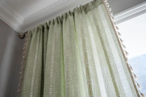Détail du rideau en lin vert avec motifs géométriques blancs et finitions à pompons crème