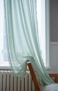 Close-up of mint green lace curtain featuring hollowed-out crochet patterns and tassels