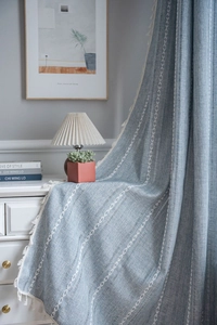 Close-up of blue linen curtain with white arrow embroidery and delicate tassel fringe