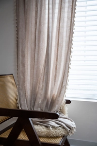Detail of bohemian cotton linen curtain with tassel edges draped over a vintage chair