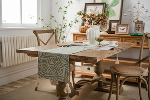 Detail of grey-green geometric woven table runner with tassels on a wooden dining table
