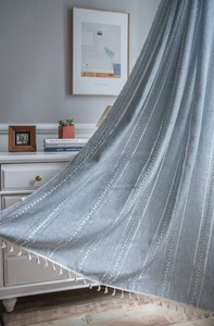 Detail of light blue textured curtain with white geometric weaving and tassel fringe