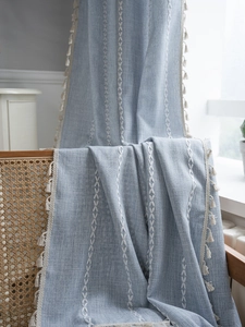 Dettaglio della tenda in lino azzurro con ricami bianchi e nappe su una sedia in legno