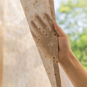 French daisy print semi-sheer linen curtain being held up to show light filtering