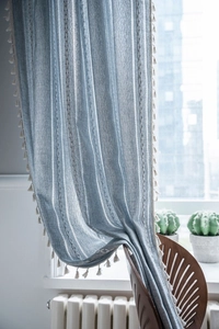 Detail of blue and white vertical striped linen curtains with off-white tassel fringe