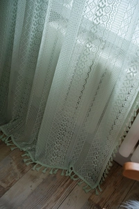 Detail of mint green crochet lace curtain with floral patterns and fringe trim at the bottom