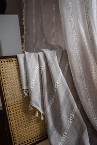 Close-up of linen curtain fabric with white embroidery stripes and fringe tassel accents