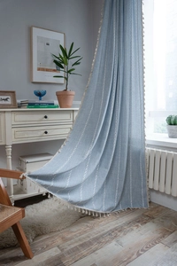 Dettaglio del tessuto misto lino azzurro con ricami geometrici bianchi e piccole nappe