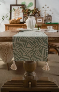 Detailed view of sage green geometric table runner with tassels on wood table