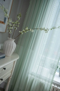 Detailed view of light green lace curtain with geometric crochet and tassel fringe