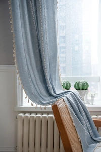 Dettaglio del tessuto in lino blu chiaro con ricamo bianco e bordo con frange a pompon