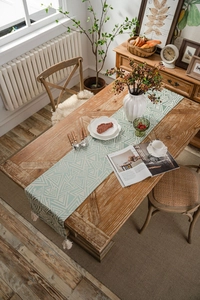 Detail of mint green geometric table runner with cotton fringes on a solid wood table