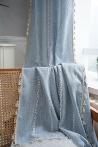 Dettaglio della tenda in lino azzurro con ricamo a chevron bianco e nappe beige
