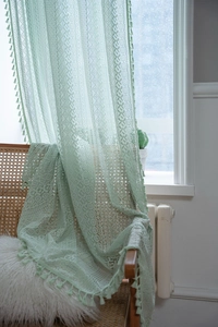 Detailed close-up of light green crochet lace curtain with geometric patterns and pompom tassels