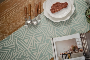 Detail of green geometric table runner with woven texture and tassels on a wooden table
