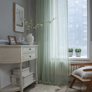 Green crochet lace curtain with geometric patterns and tassels in a rustic living room