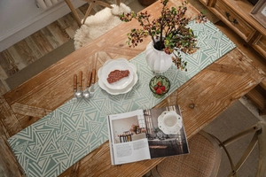 Detail of green geometric table runner with white triangles and tassels on a wooden table