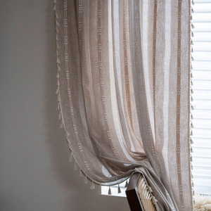 Boho beige striped semi-sheer linen curtain with tassels displayed on a chair