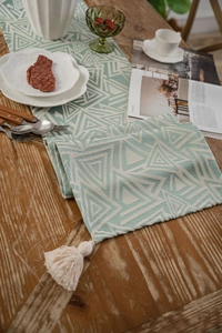 Detail of green geometric pattern table runner with creamy cotton tassels on wood table