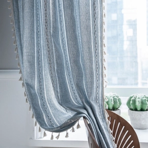Blue striped cotton linen curtain with beige tassels in a cozy sunlit room setting