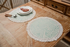 Close-up of green geometric round placemats with white crochet lace trim on a wooden table