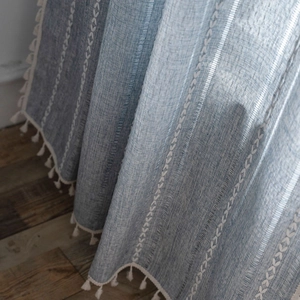 Country style blue striped linen curtain with white embroidery and cotton tassels on wood floor