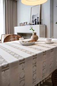 Close-up of cream rectangular tablecloth with hollow lace, diamond pattern and tassels