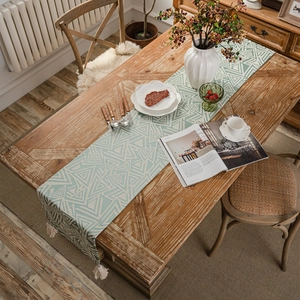Modern geometric green table runner with beige tassels on a rustic wooden dining table