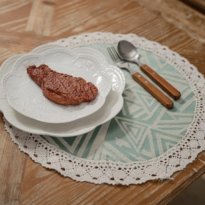 Modern mint green geometric woven placemat with white lace trim on wooden table