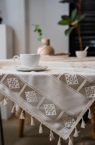 Detailed close-up of beige crochet lace tablecloth with hollow patterns and fringe