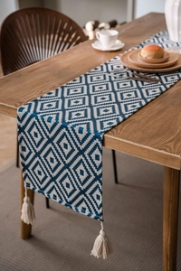 Detail of blue geometric jacquard runner with cream tassels on a wooden dining table
