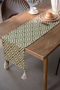 Close-up of green geometric jacquard table runner with decorative cotton tassels