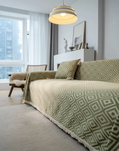 Close-up of green geometric jacquard sofa cover with decorative tassel fringe details