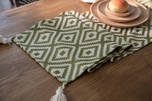 Detail of green geometric diamond pattern table runner with white woven tassels on wood