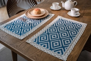 Detail of blue geometric jacquard placemats with white crochet lace trim on a wood table