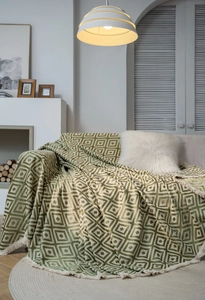 Detail of green geometric jacquard sofa throw with thick woven texture and decorative tassels